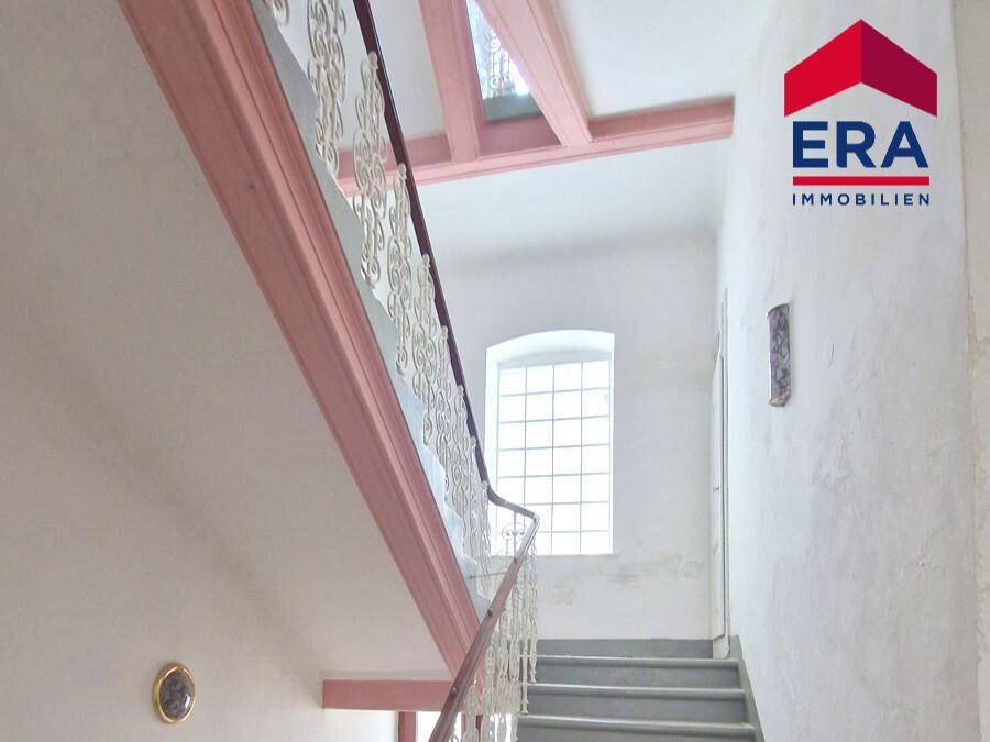 Treppenhaus mit schmiedeeisernem Geländer, hohen Decken und einem Fenster für Tageslicht.