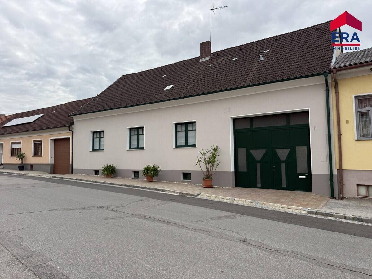 Ansicht des Einfamilienhauses von der Straße mit Garagentor und Fenstern.