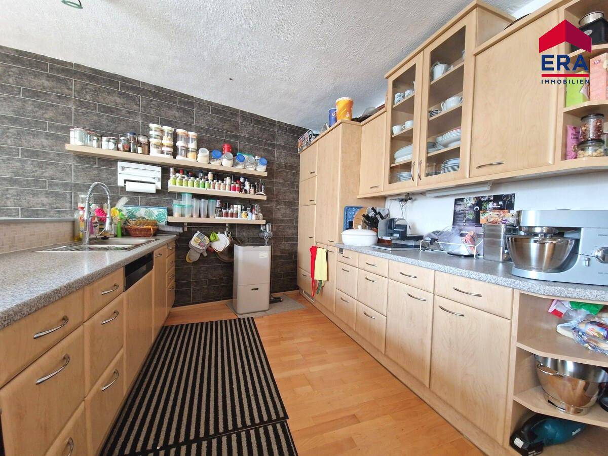 Funktionale Küche mit hellen Holzschränken, Granitarbeitsplatten und Fliesen an der Wand.