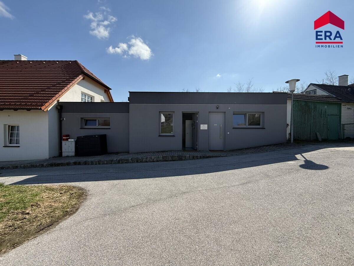 Moderne graue Gebäudefassade mit Fenstern und Eingangstür unter blauem Himmel.
