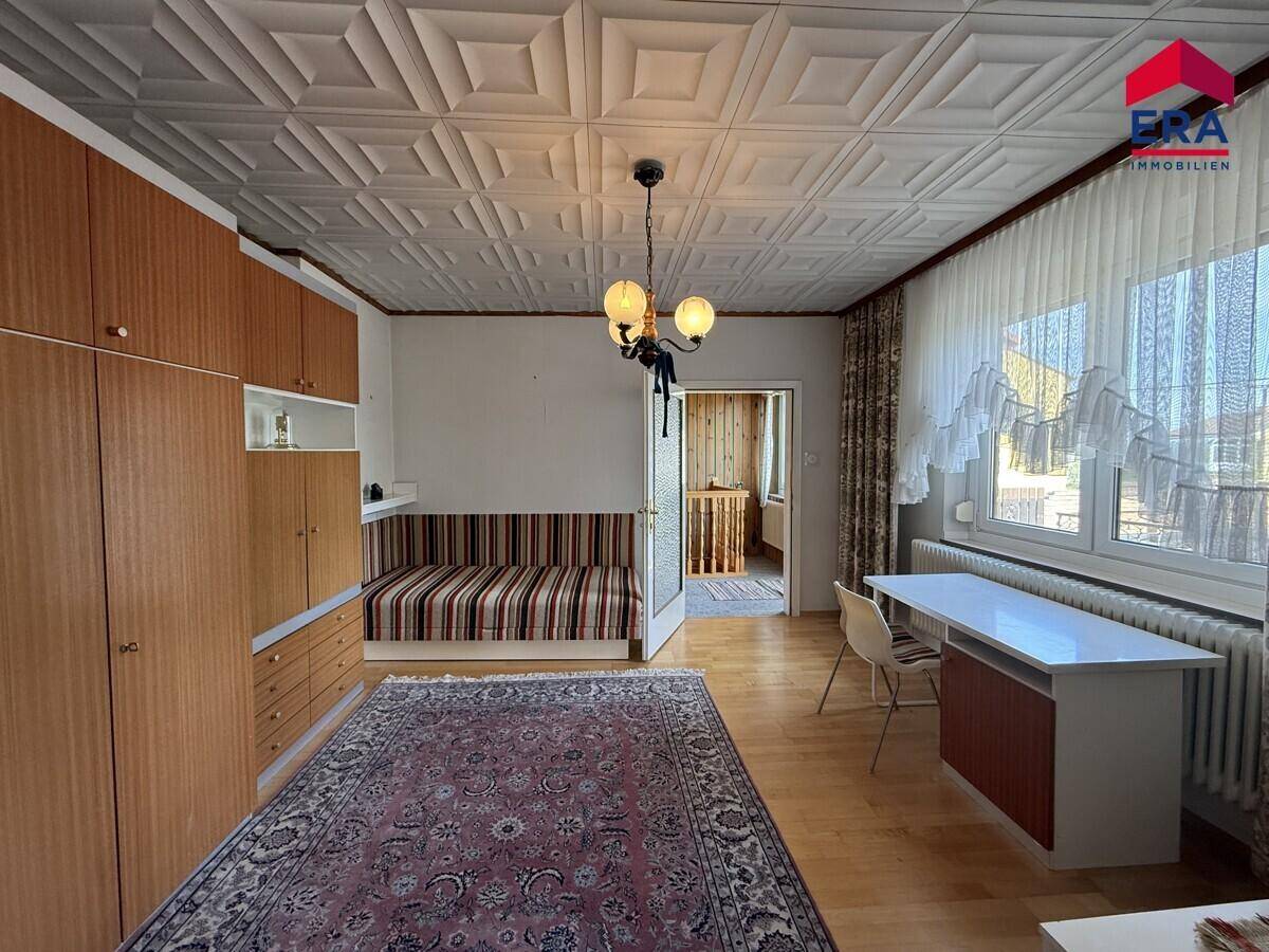 Helles Schlafzimmer mit Holzfußboden, Tagesbett und einem Schreibtisch am Fenster.