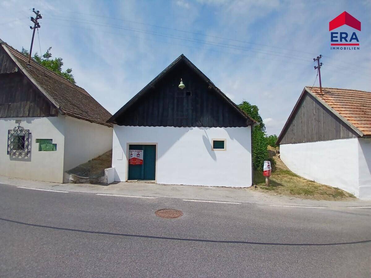 Nahaufnahme eines traditionellen Gebäudes mit weißer Fassade und dunklem Giebeldach an einer sonnigen Straße.