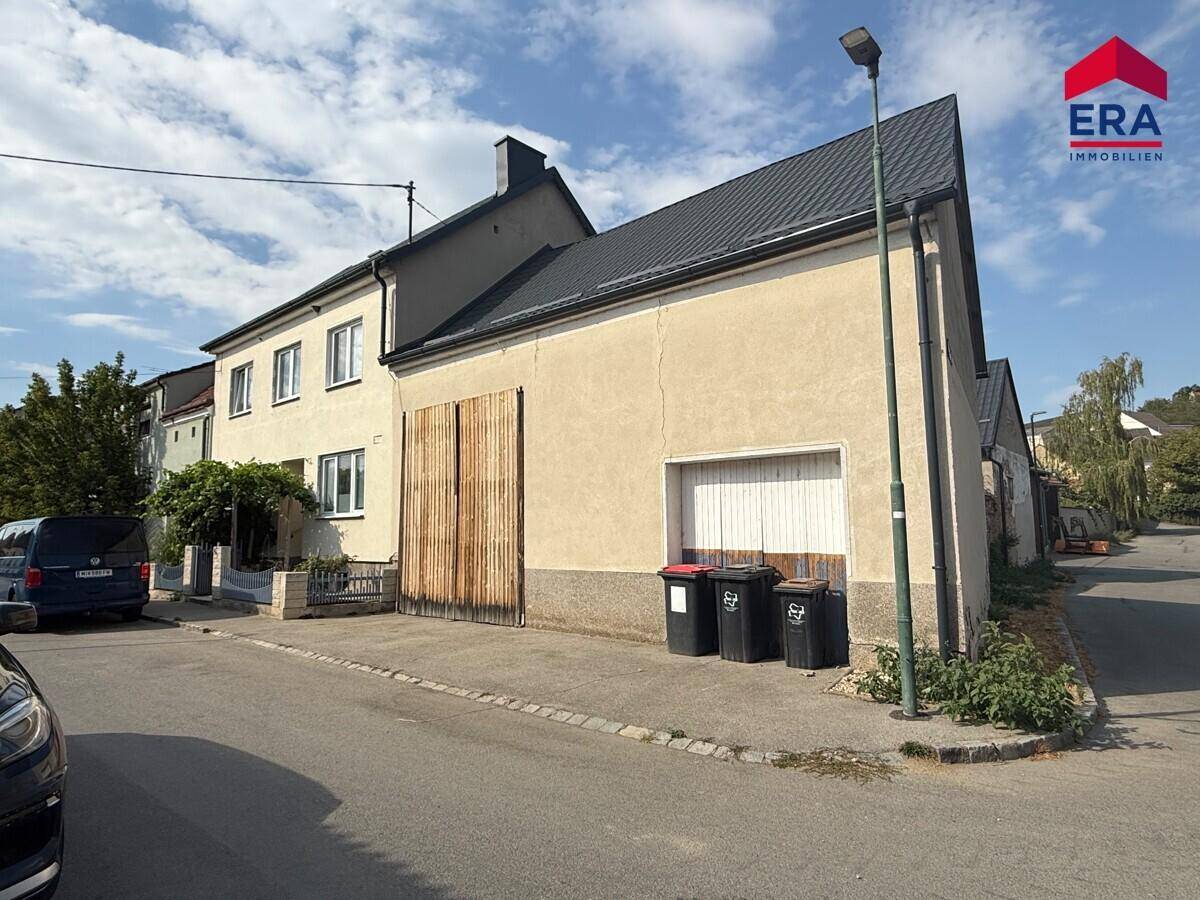 Seitenansicht des Gebäudes von der Straße mit großen Holztoren und Mülltonnen.