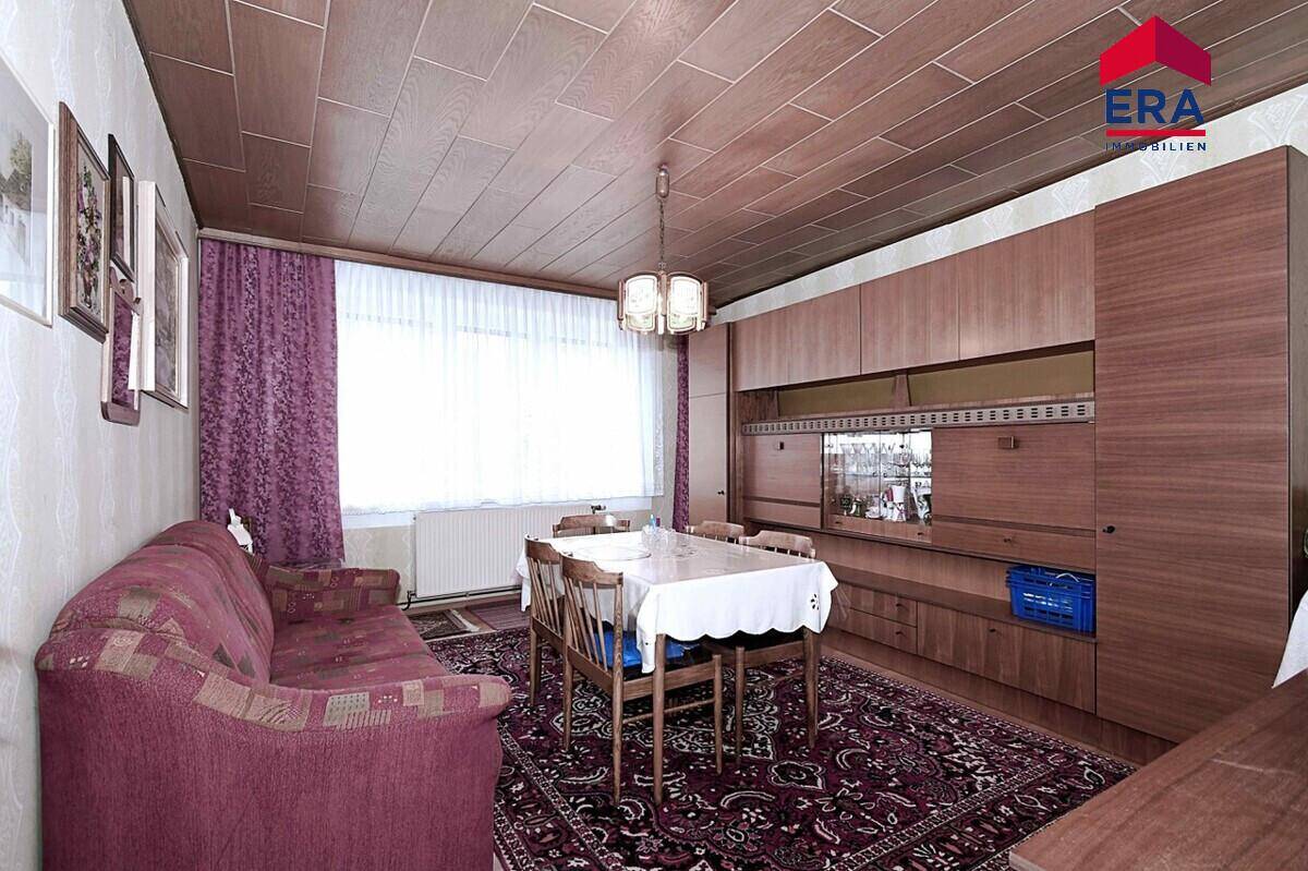 Wohn- und Essbereich mit Holzpaneeldecke, Teppichboden und traditionellen Möbeln.