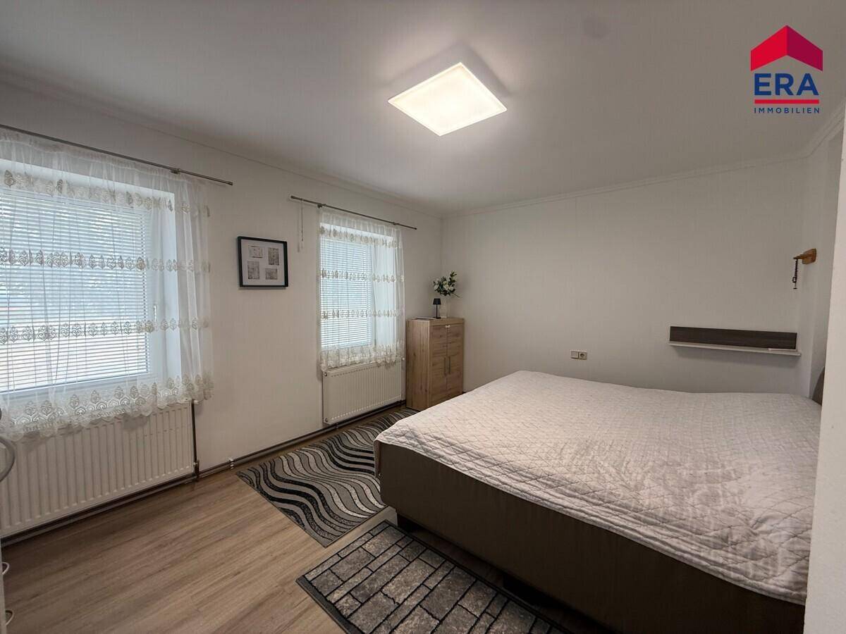 Helles Schlafzimmer mit Doppelbett, zwei Fenstern und modernem Laminatboden.
