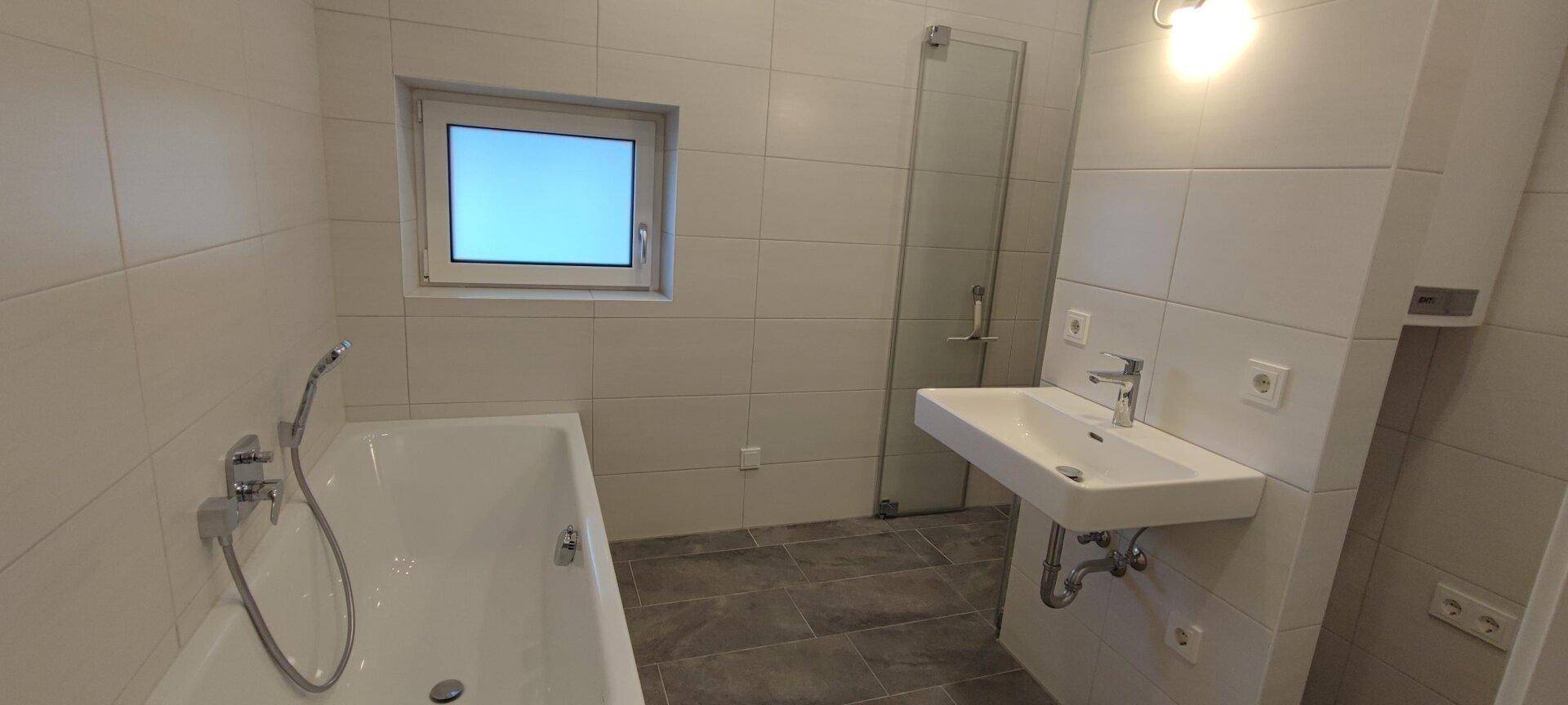 Modernes Badezimmer mit weißen Wandfliesen, dunklem Boden und Badewanne mit Duschfunktion.