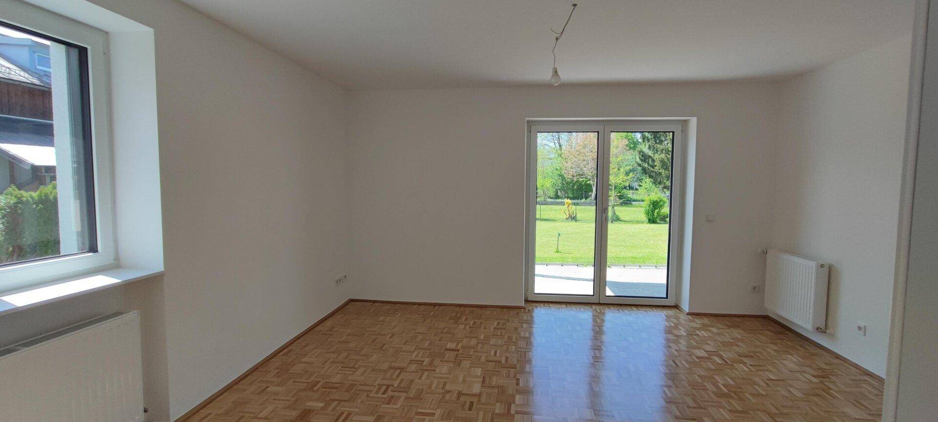 Geräumiges, leeres Wohnzimmer mit Parkettboden und großer Terrassentür zum Garten.