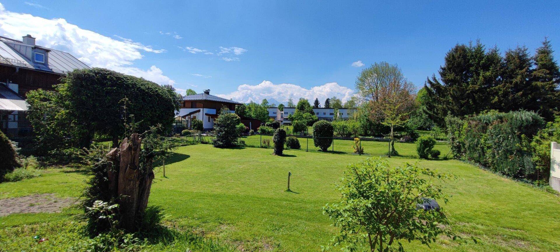 Großer, gepflegter Garten mit Rasenfläche, Bäumen und Blick auf die Berge.