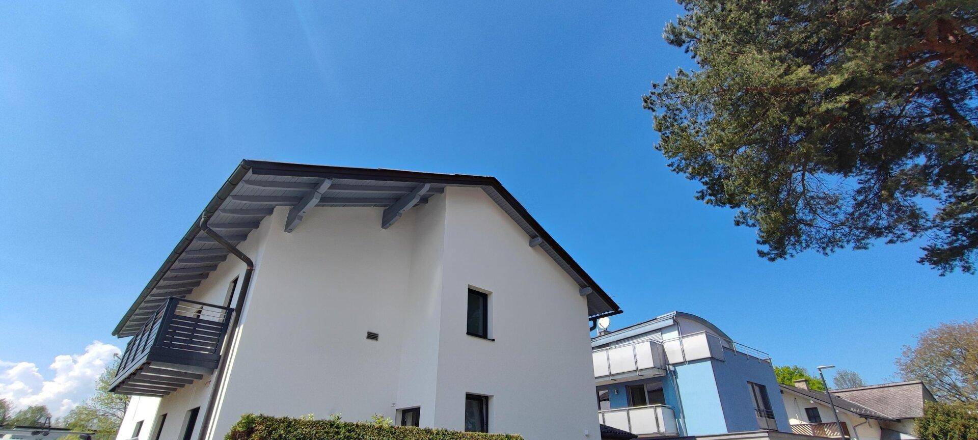 Ansicht des Hauses mit Satteldach und Balkon unter strahlend blauem Himmel.