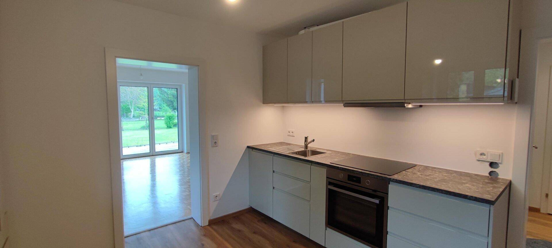 Helle Küche mit Spüle, Kochfeld und Ofen, bietet direkten Zugang zum Gartenbereich.