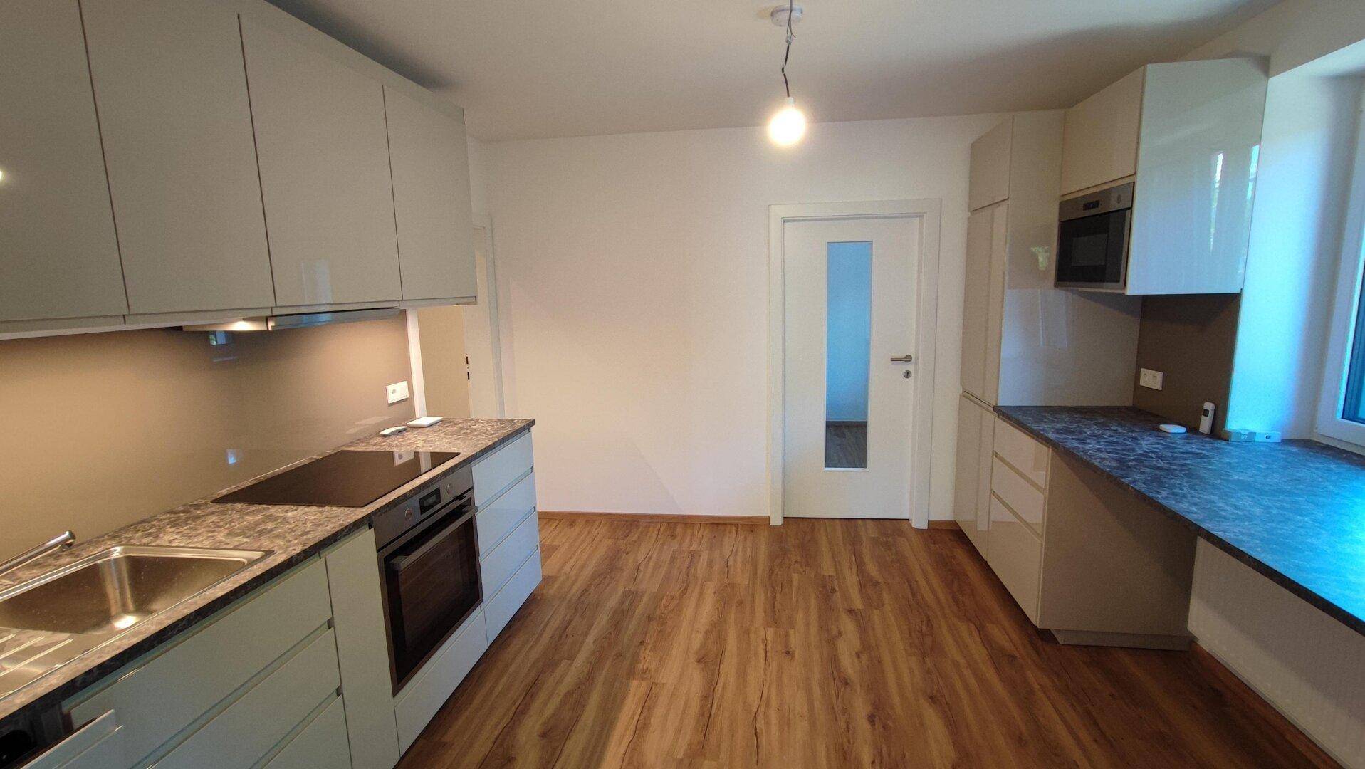 Moderne Küche mit hellgrauen Hochglanzfronten, dunkler Arbeitsplatte und Holzboden.