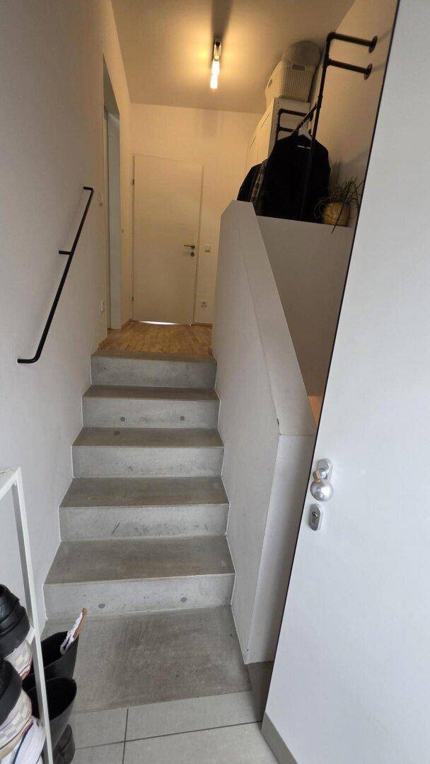 Heller Treppenaufgang mit Betonstufen und weiß gestrichenen Wänden, der zu einer oberen Etage führt.