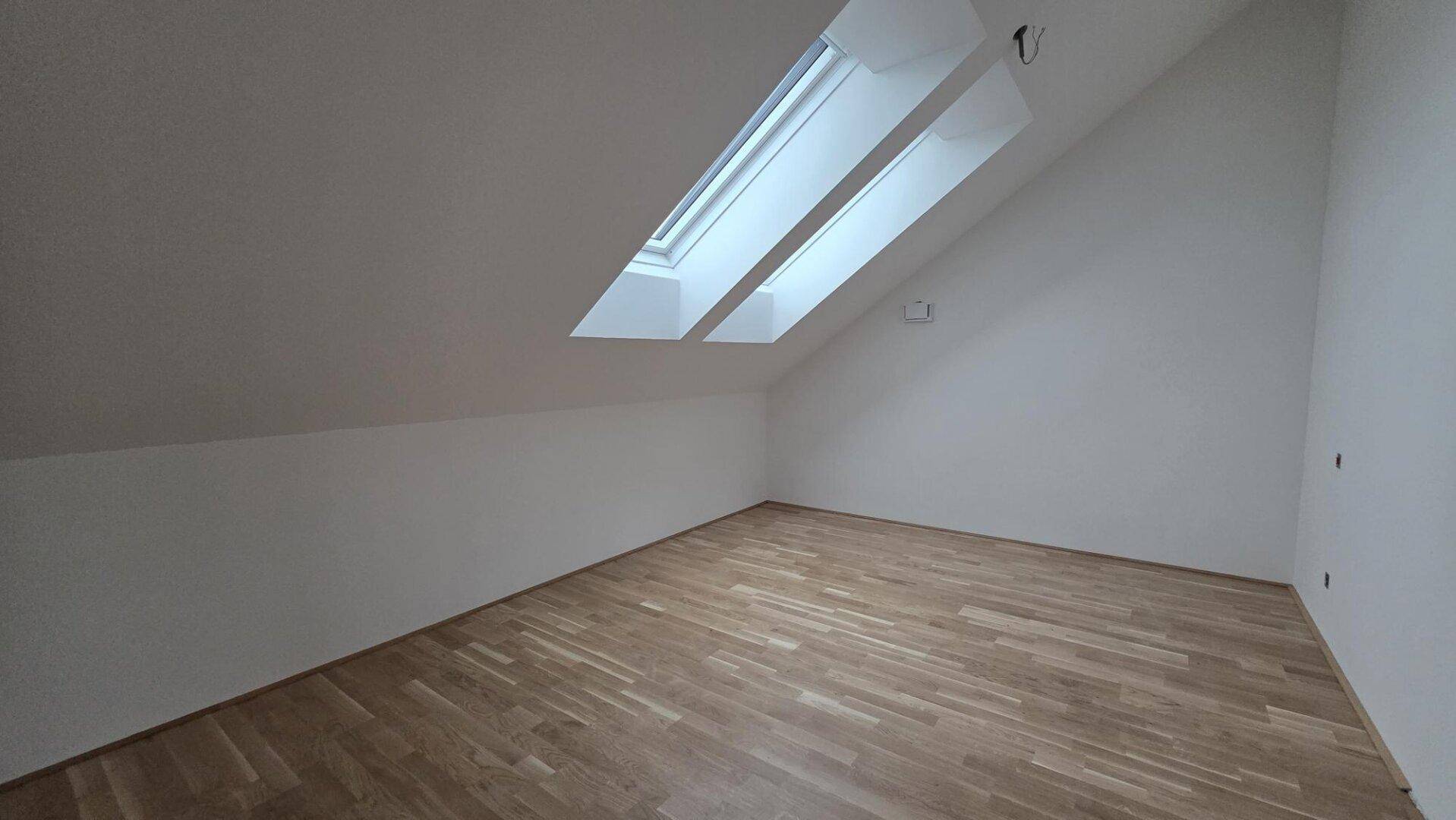 Heller Raum im Dachgeschoss mit Parkettboden und zwei Dachfenstern für viel Tageslicht.