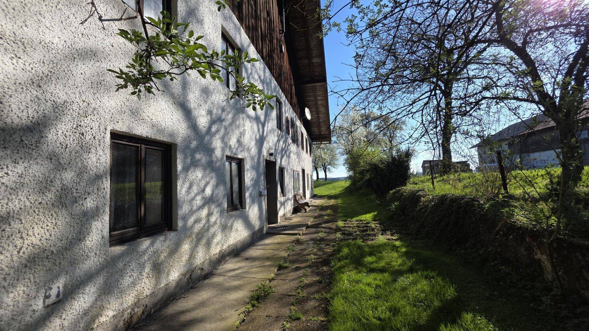 Seitenansicht eines ländlichen Gebäudes mit kleinen Fenstern und einem schmalen Pfad entlang der Fassade.