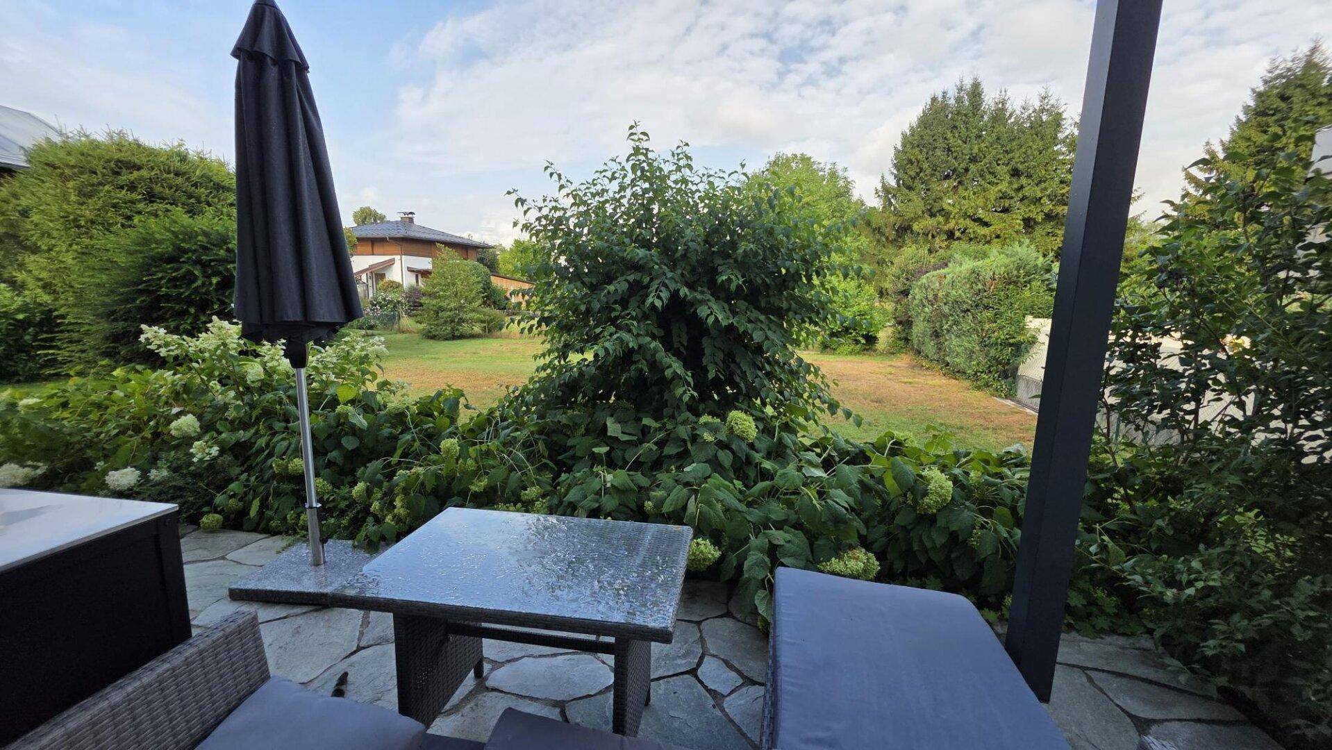 Gemütlicher Außenbereich mit Terrasse, Sitzgelegenheiten und Blick in den grünen Garten.