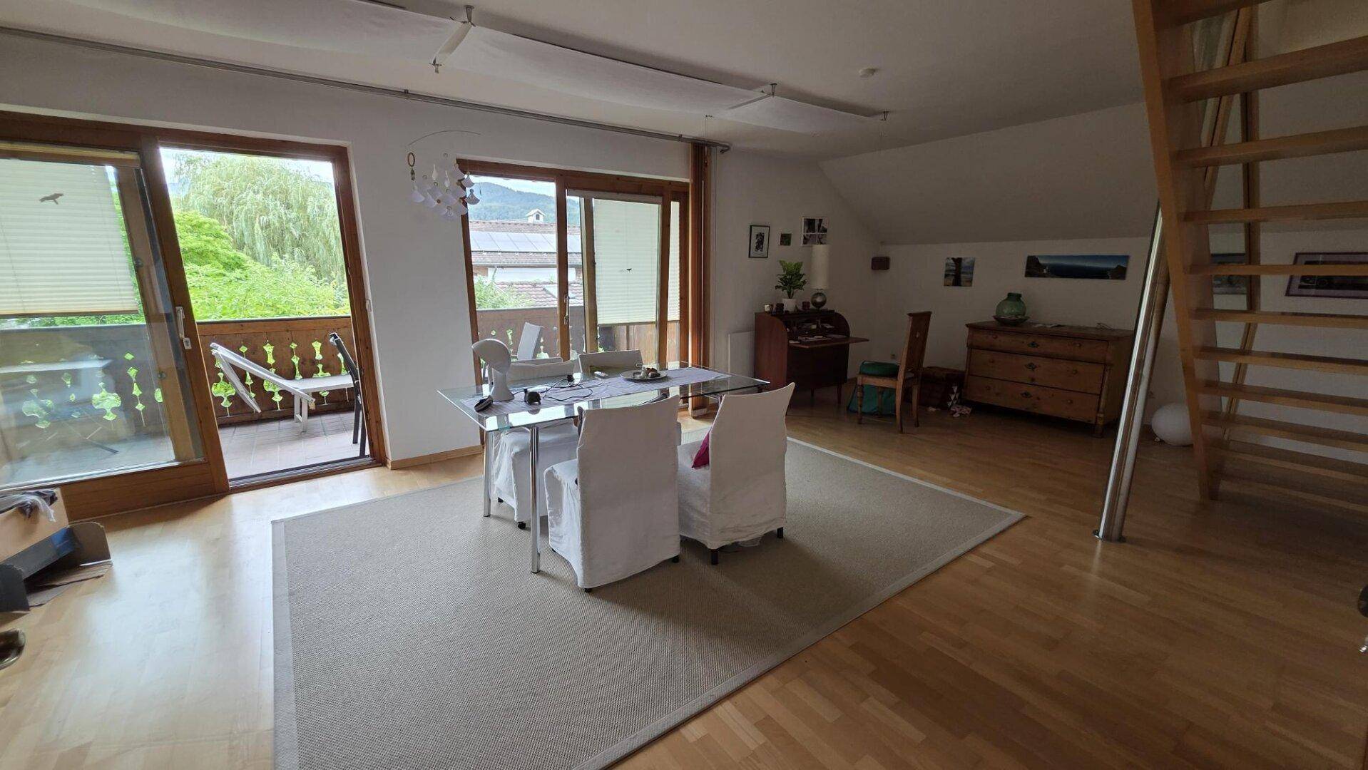 Heller Essbereich mit Holzboden und großen Fenstern, die Zugang zu einem Balkon bieten.