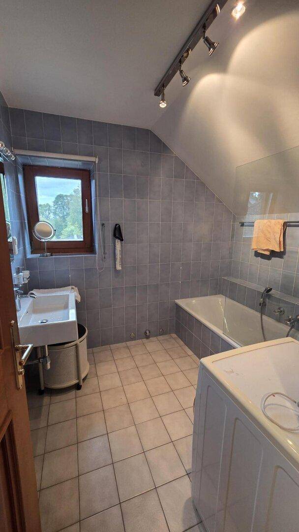 Badezimmer mit blauen Fliesen, Badewanne, Waschbecken und einem Fenster unter der Dachschräge.