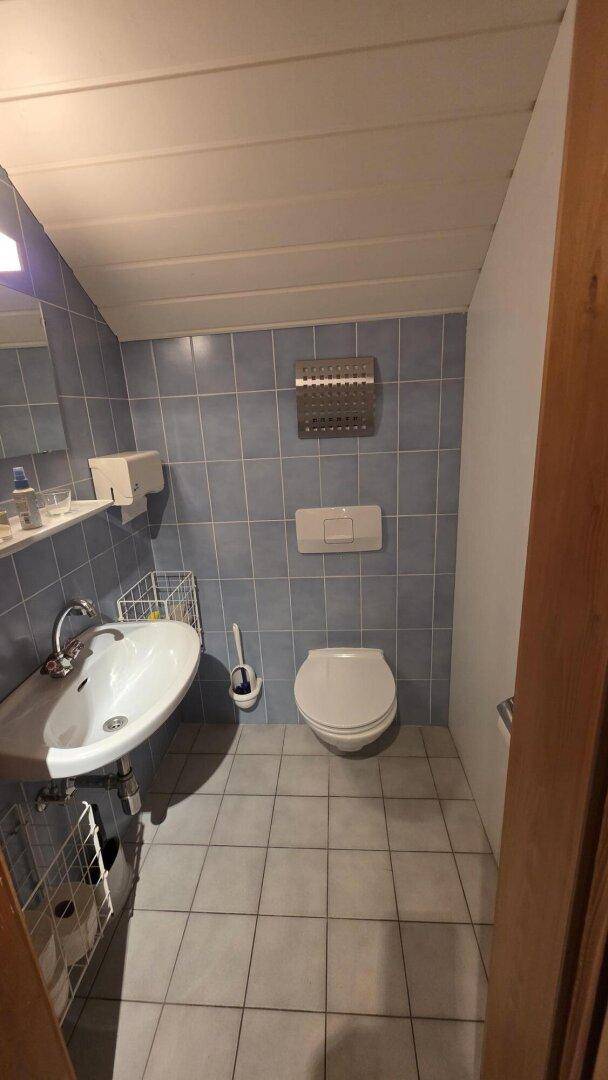 Kleines WC mit blauen Wand- und Bodenfliesen, Waschbecken und wandhängender Toilette.