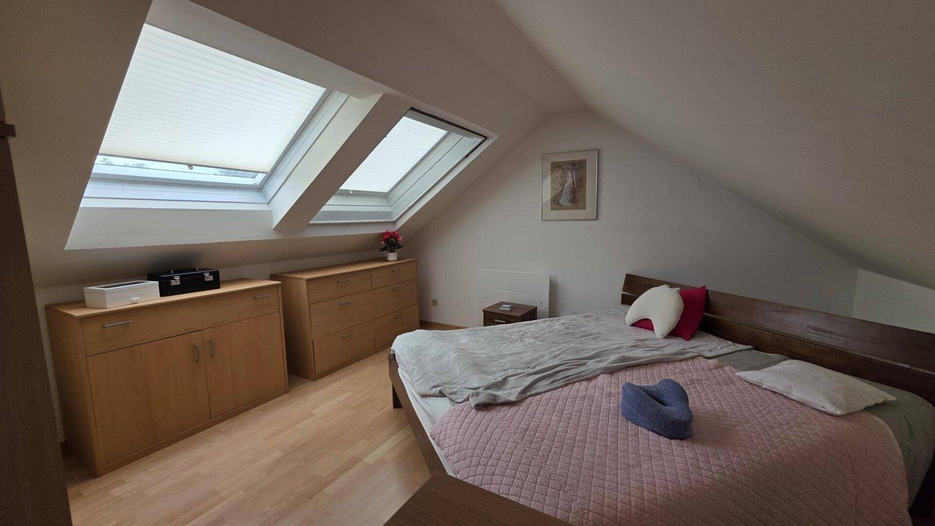 Gemütliches Schlafzimmer mit Holzboden, Dachschräge und zwei Dachfenstern für natürliches Licht.