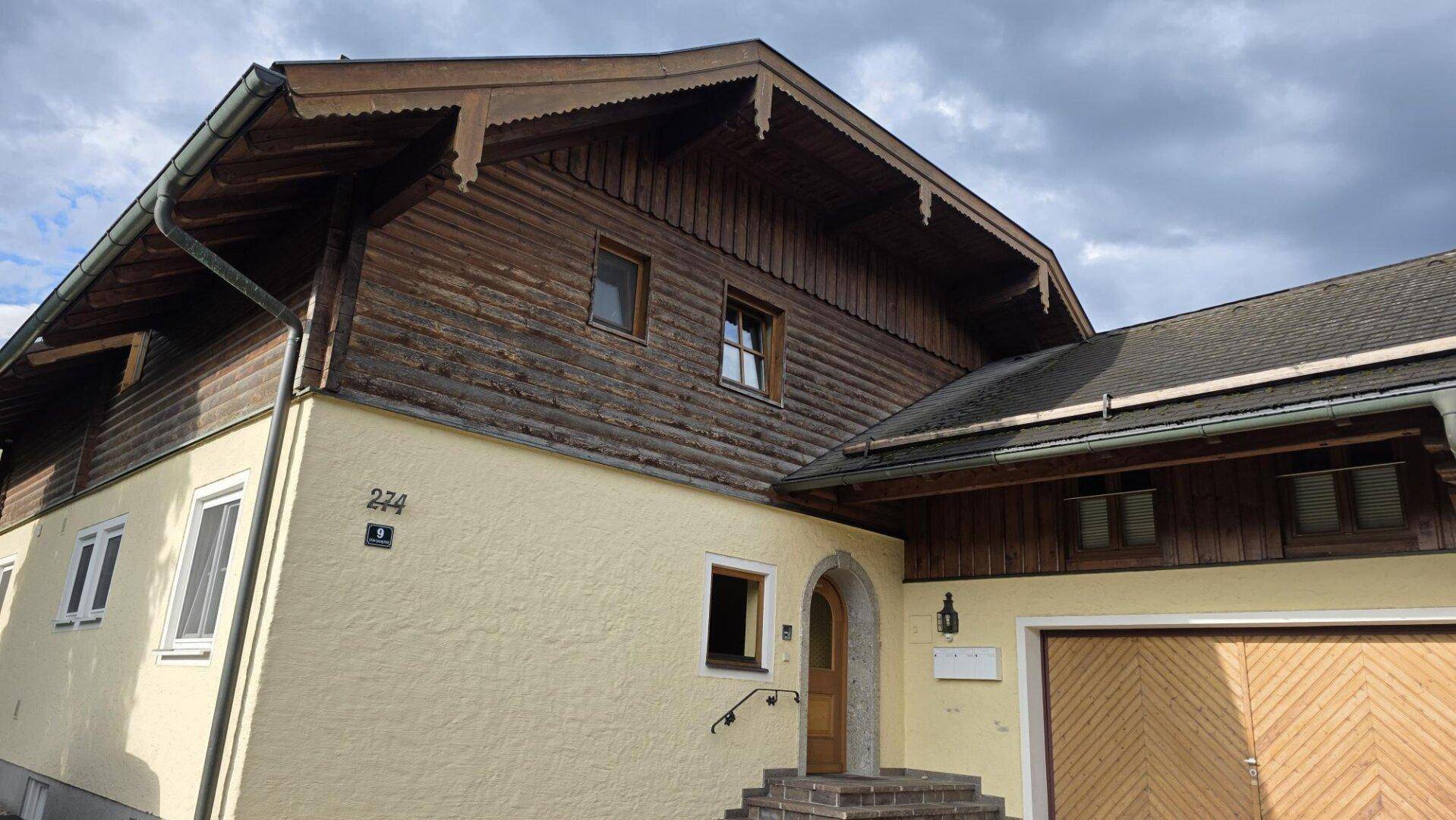 Traditionelles Haus mit Holzfassade im oberen Bereich und hellem Putz im unteren Bereich, inklusive Garage.