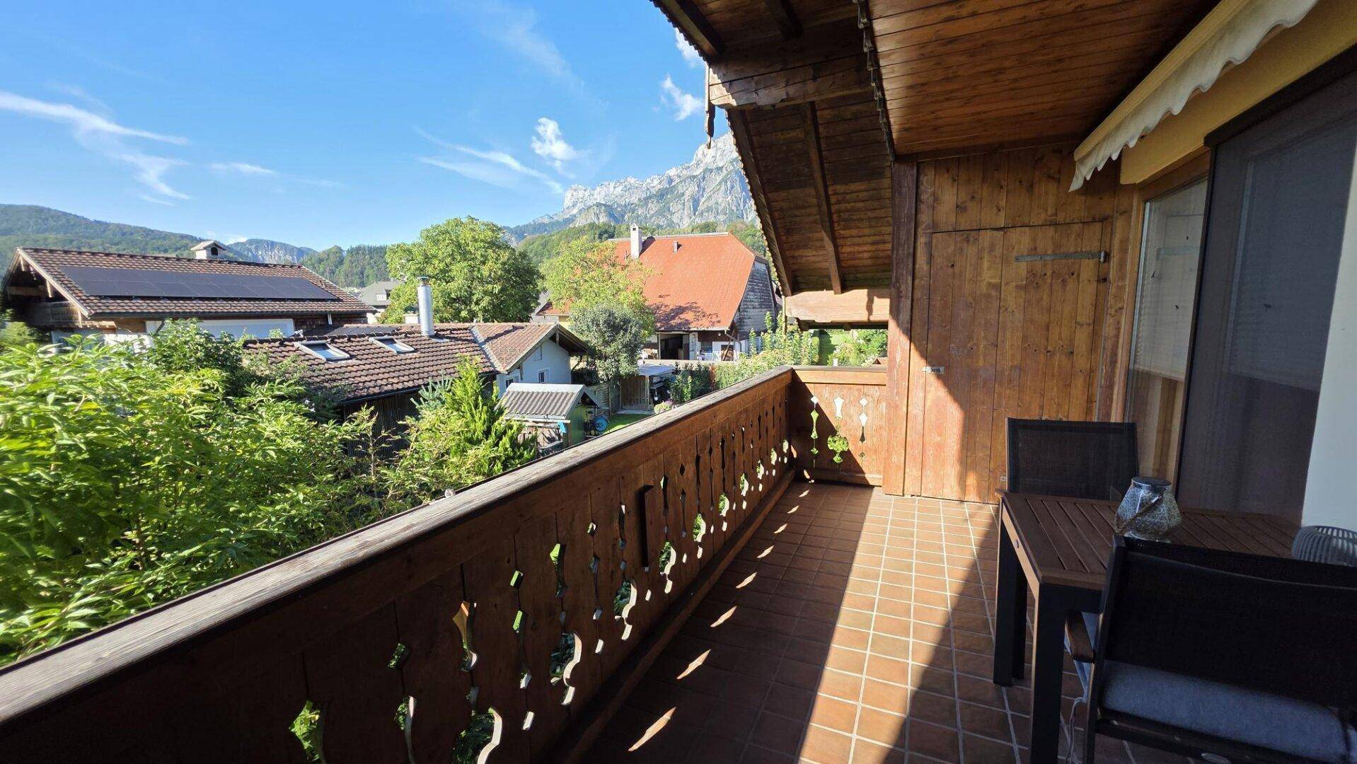 Sonniger Holzbalkon mit Bergblick und Sitzgelegenheiten, umgeben von grüner Natur.