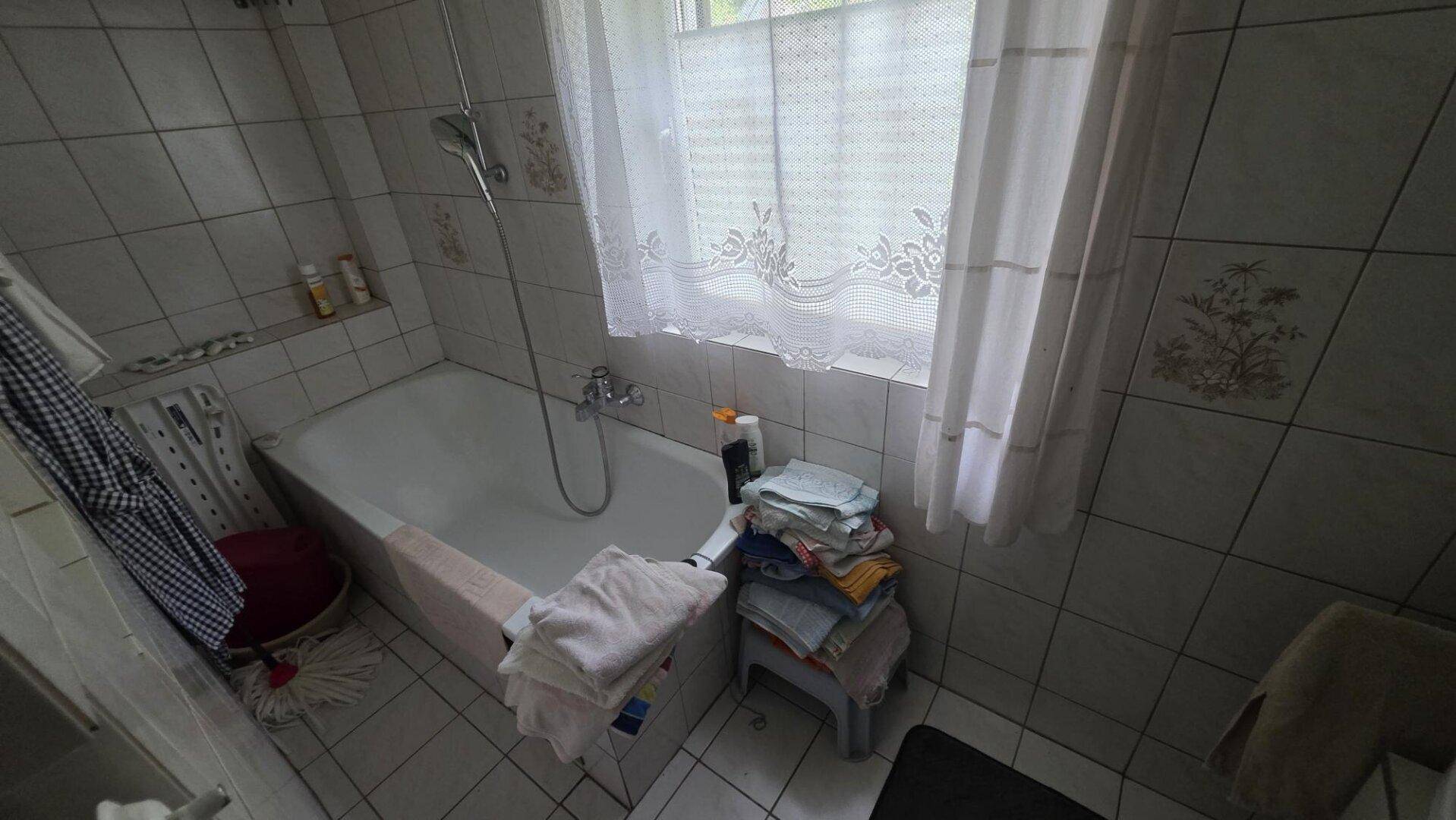 Badezimmer mit Badewanne, gefliesten Wänden und einem Fenster, das Tageslicht hereinlässt.