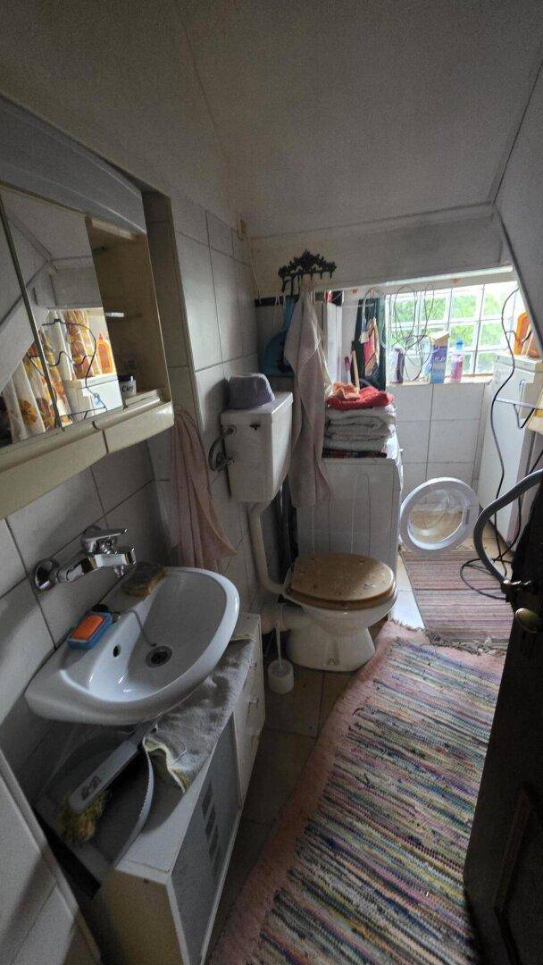 Kleines Badezimmer mit Waschbecken, Toilette und Waschmaschine unter dem Fenster.