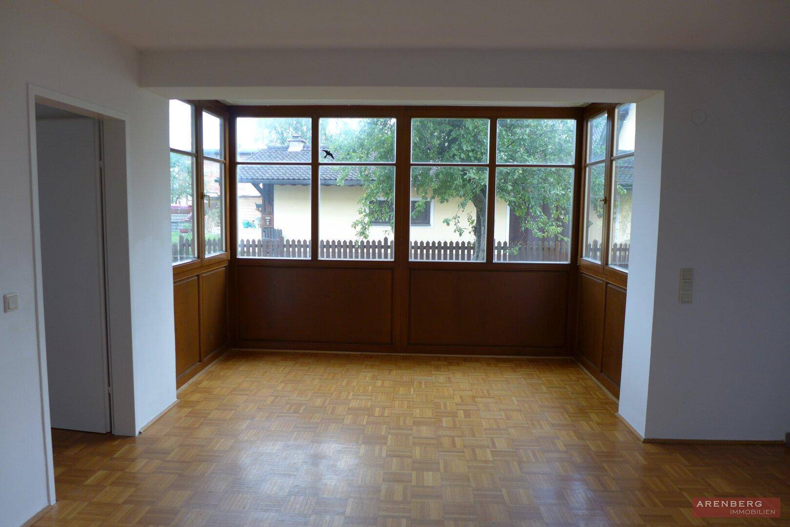 Helles Wohnzimmer mit Parkettboden und großem Fensterbereich, der viel Tageslicht hereinlässt.