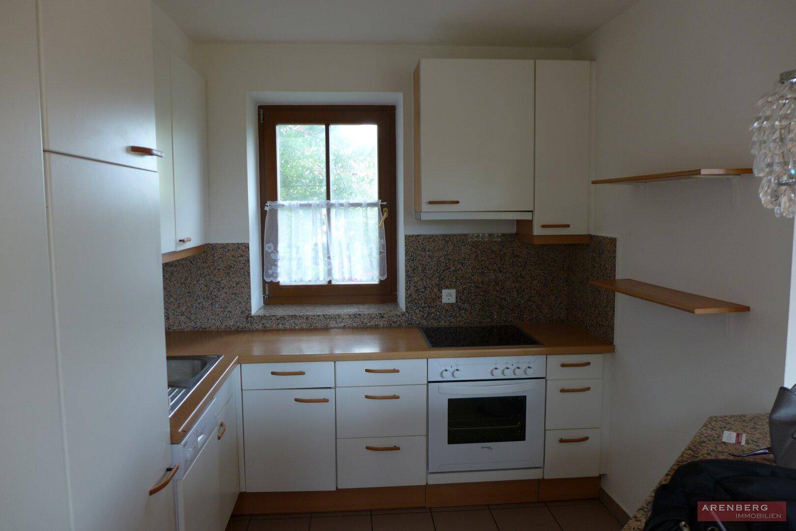 Funktionale Küche mit weißen Schränken, Holztheke und Fenster mit Blick ins Grüne.