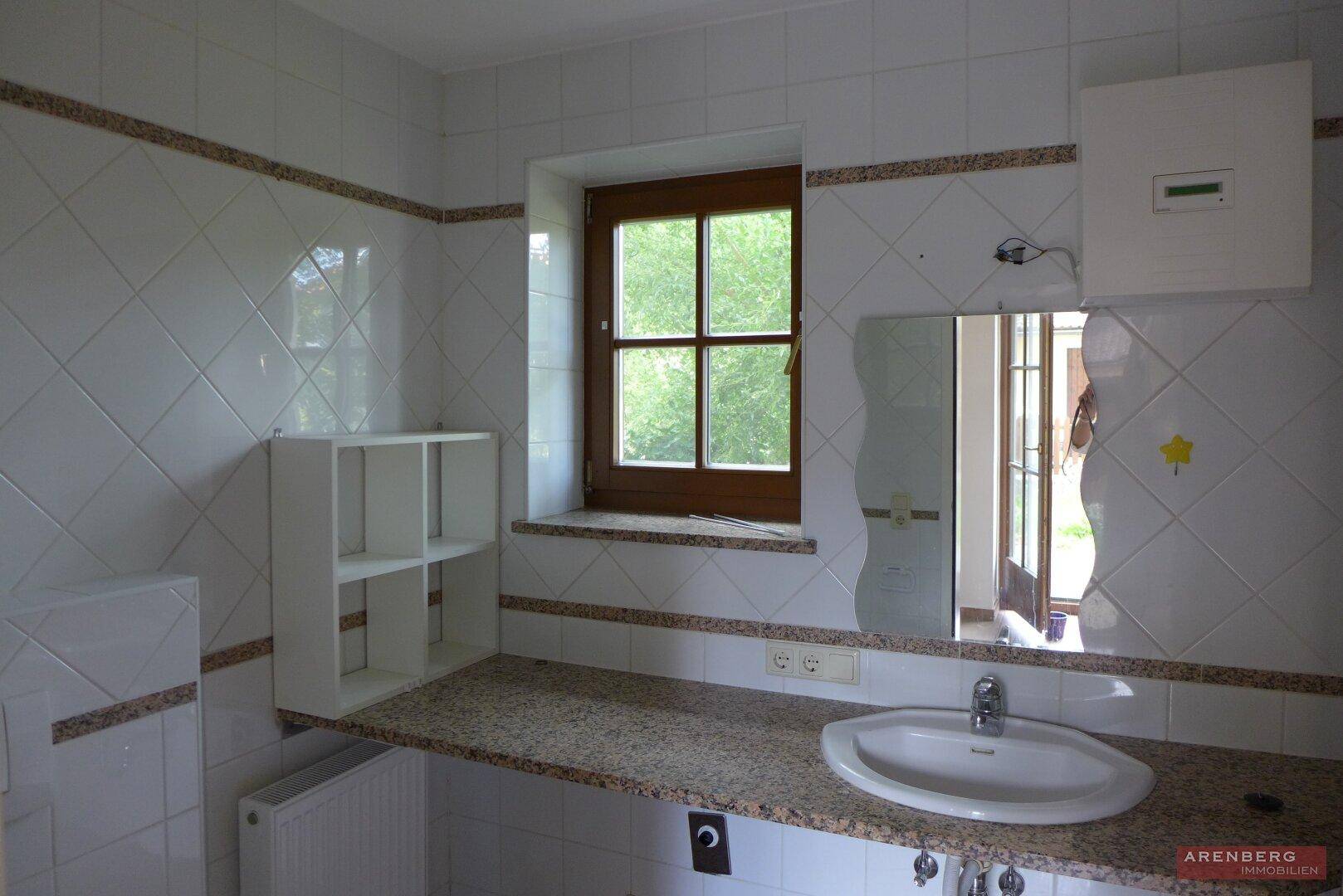 Gefliestes Badezimmer mit Einzelwaschbecken, Spiegelschrank und Fenster für Tageslicht.