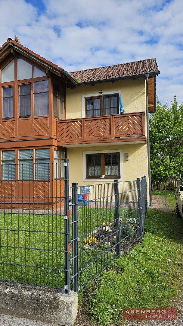 Ansicht des Hauses mit Balkon, Wintergarten und neuem Metallzaun im Vorgarten unter blauem Himmel.
