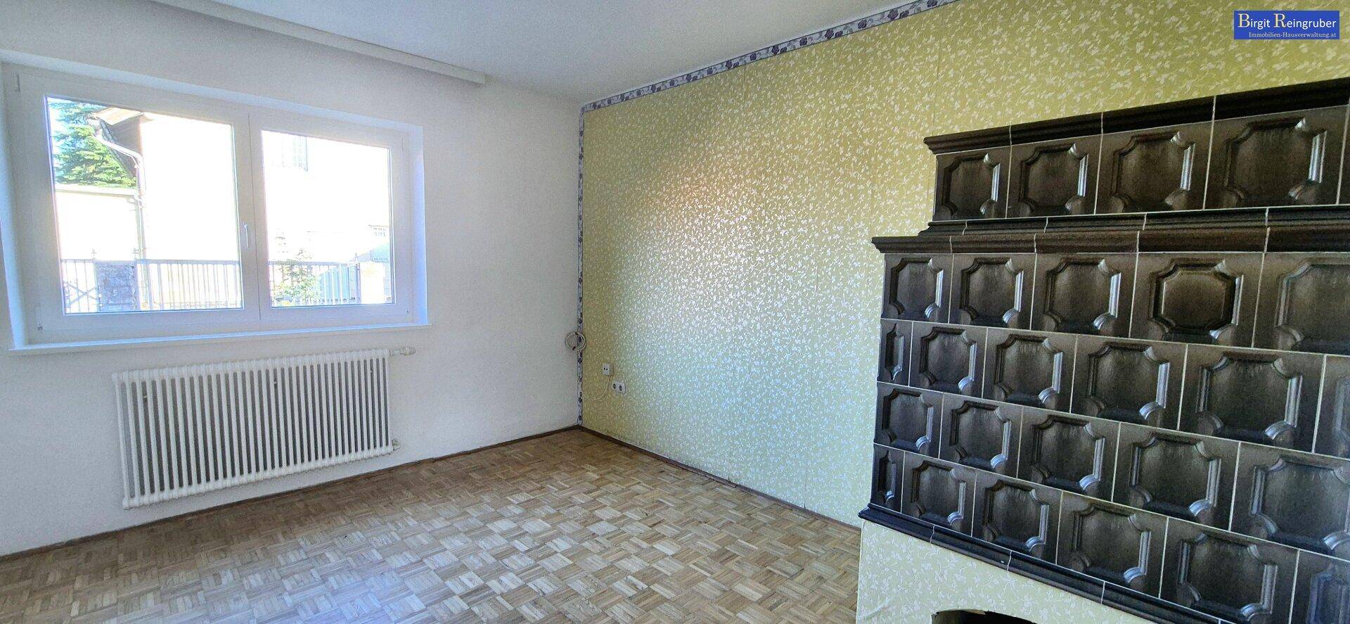 Gemütlicher Raum mit traditionellem Kachelofen, Parkettboden und Fenster.