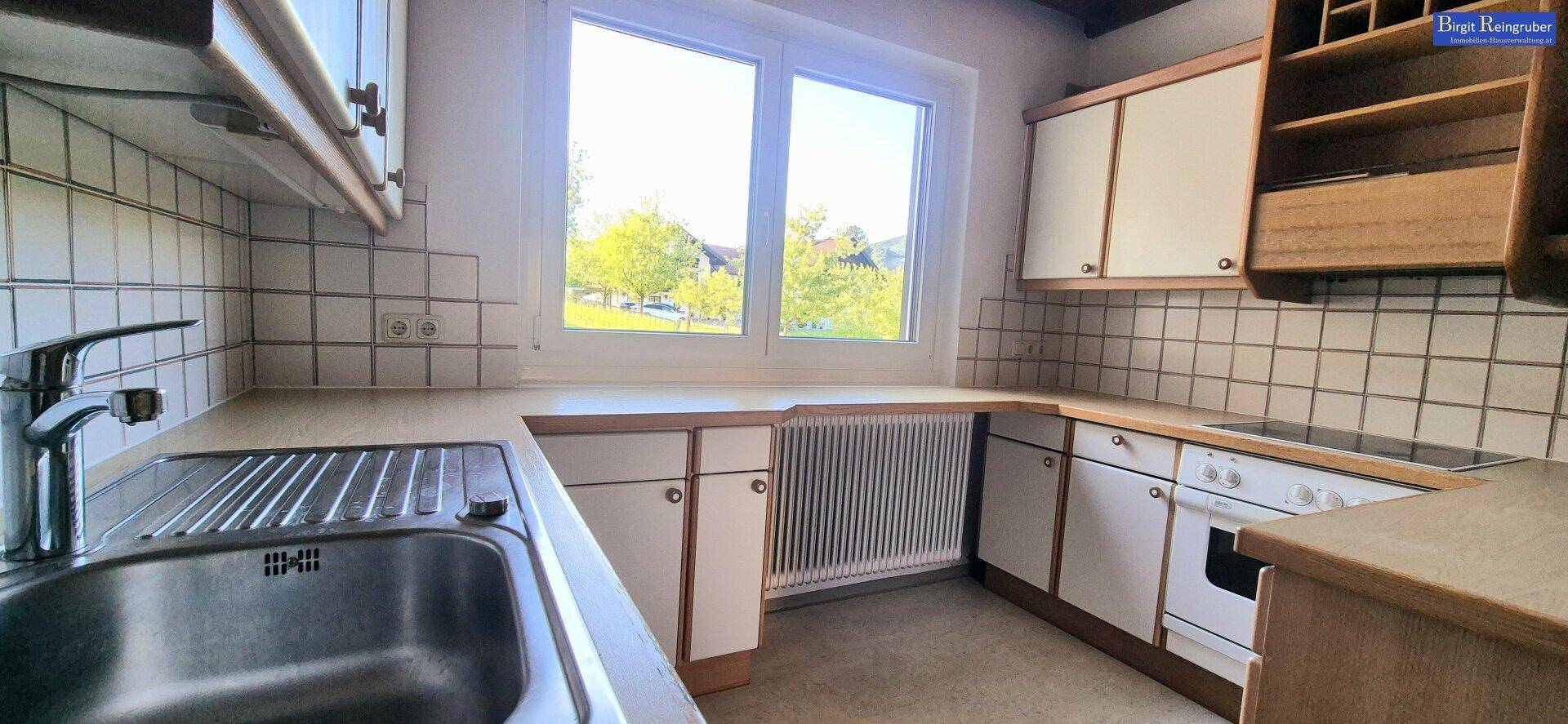Funktionale Küche mit weißen Schränken, Fliesenrückwand und Fenster mit Grünblick.