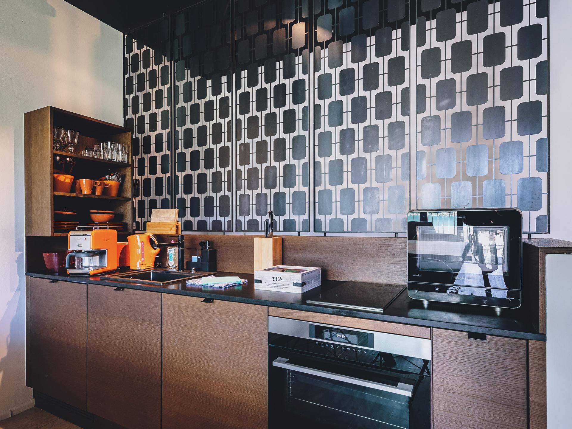 Moderne Küche mit dunklen Holzfronten, integrierten Geräten und einer stilvollen gemusterten Rückwand.