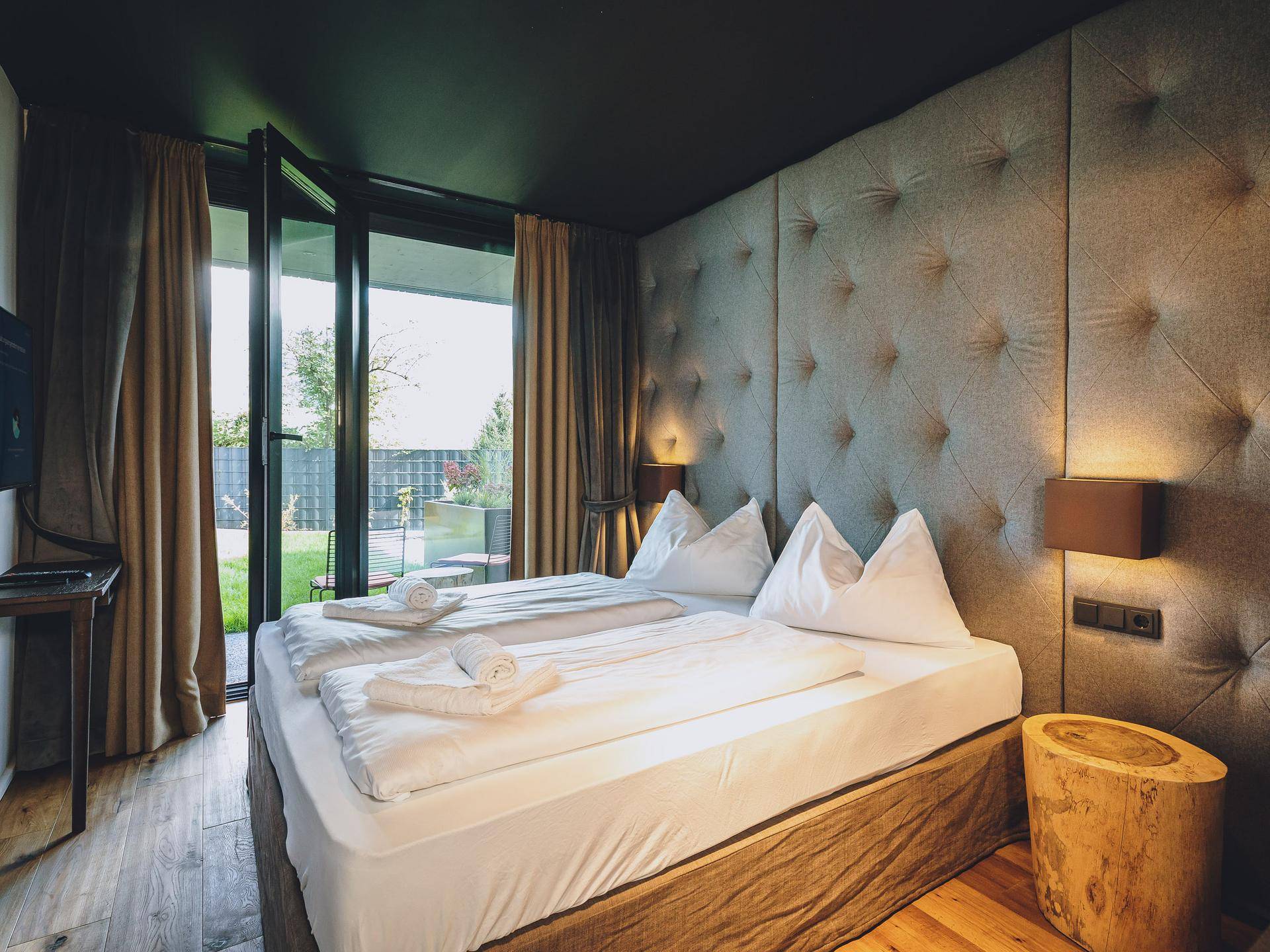 Gemütliches Schlafzimmer mit großem Bett, Holzboden und direktem Zugang zu einem kleinen Gartenbereich.