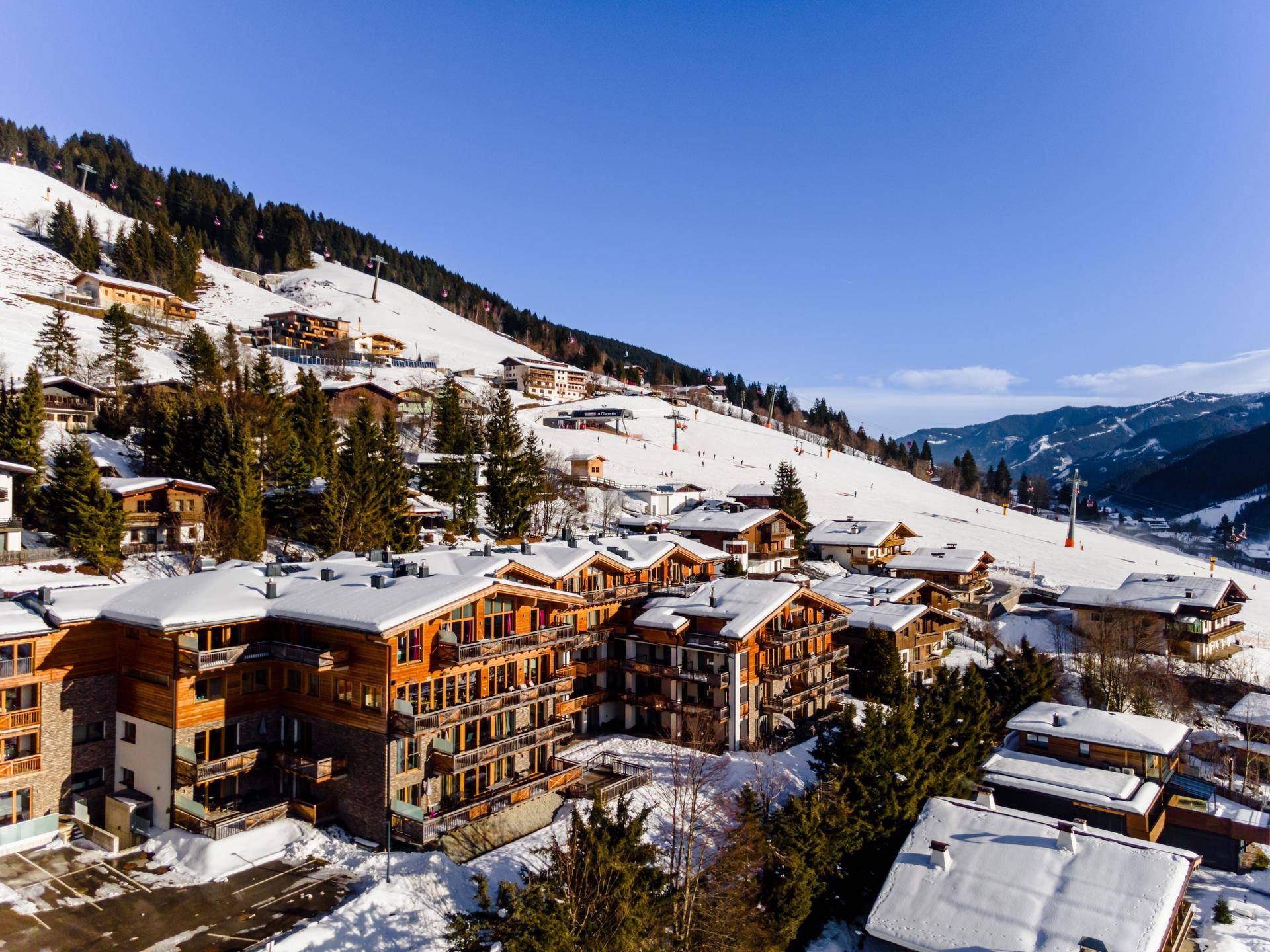 Winterliche Ansicht von modernen Gebäuden in einer verschneiten Berglandschaft mit Skipisten.