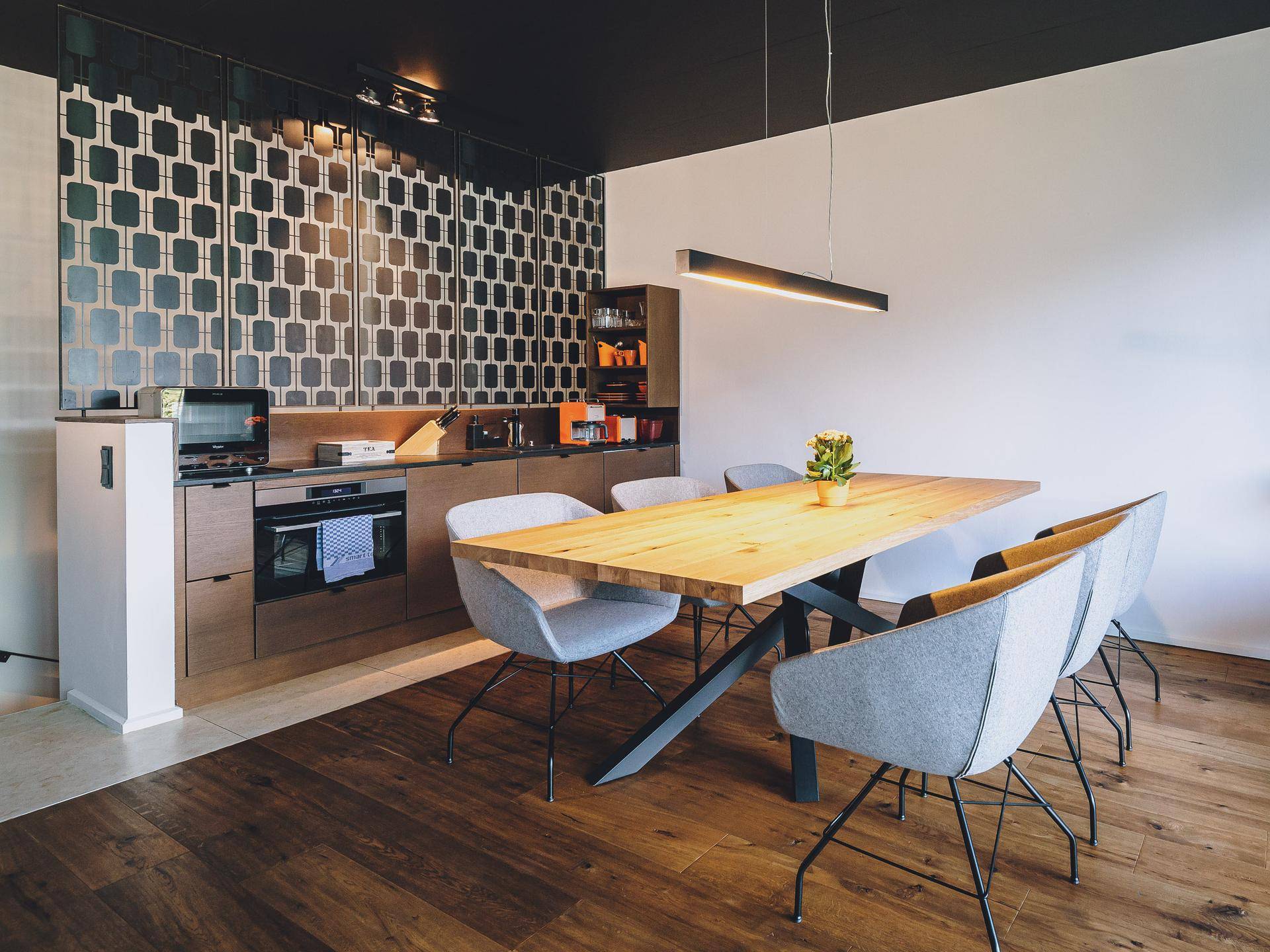 Moderne Küche mit Holzboden, integrierten Geräten und großem Esstisch.