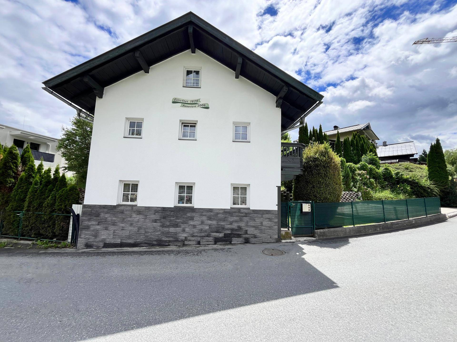 Seitenansicht eines traditionellen Hauses mit weißer Fassade, Satteldach und grüner Umgebung.