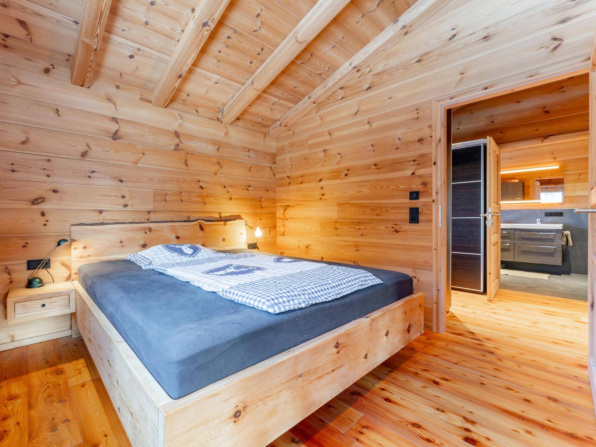 Gemütliches Schlafzimmer mit Holzböden und -wänden, Holzbett und Zugang zum modernen Badezimmer.