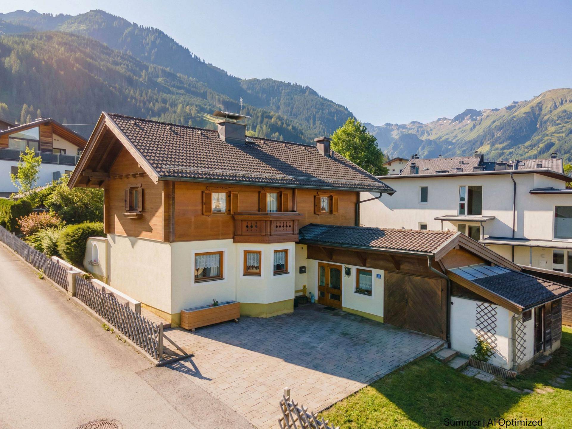Traditionelles Haus mit Holzfassade, Satteldach und gepflasterter Einfahrt in alpiner Umgebung.