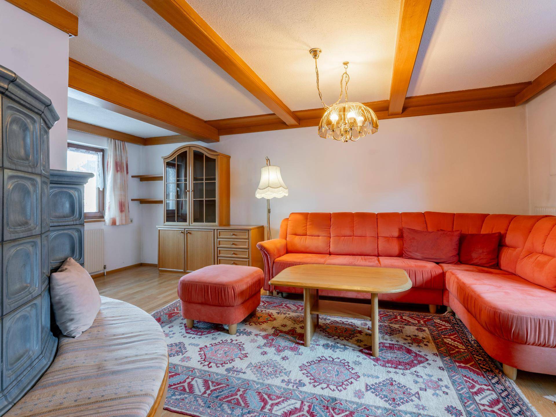 Helles Wohnzimmer mit traditionellem Kachelofen, Holzbalken und gemütlicher Sitzecke.