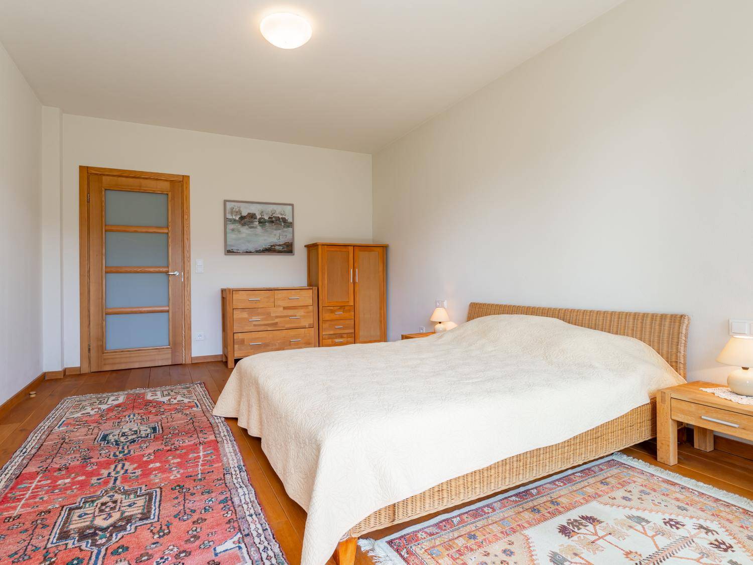 Schlafzimmer mit Doppelbett, Holzmöbeln und traditionellen Teppichen auf Holzboden.