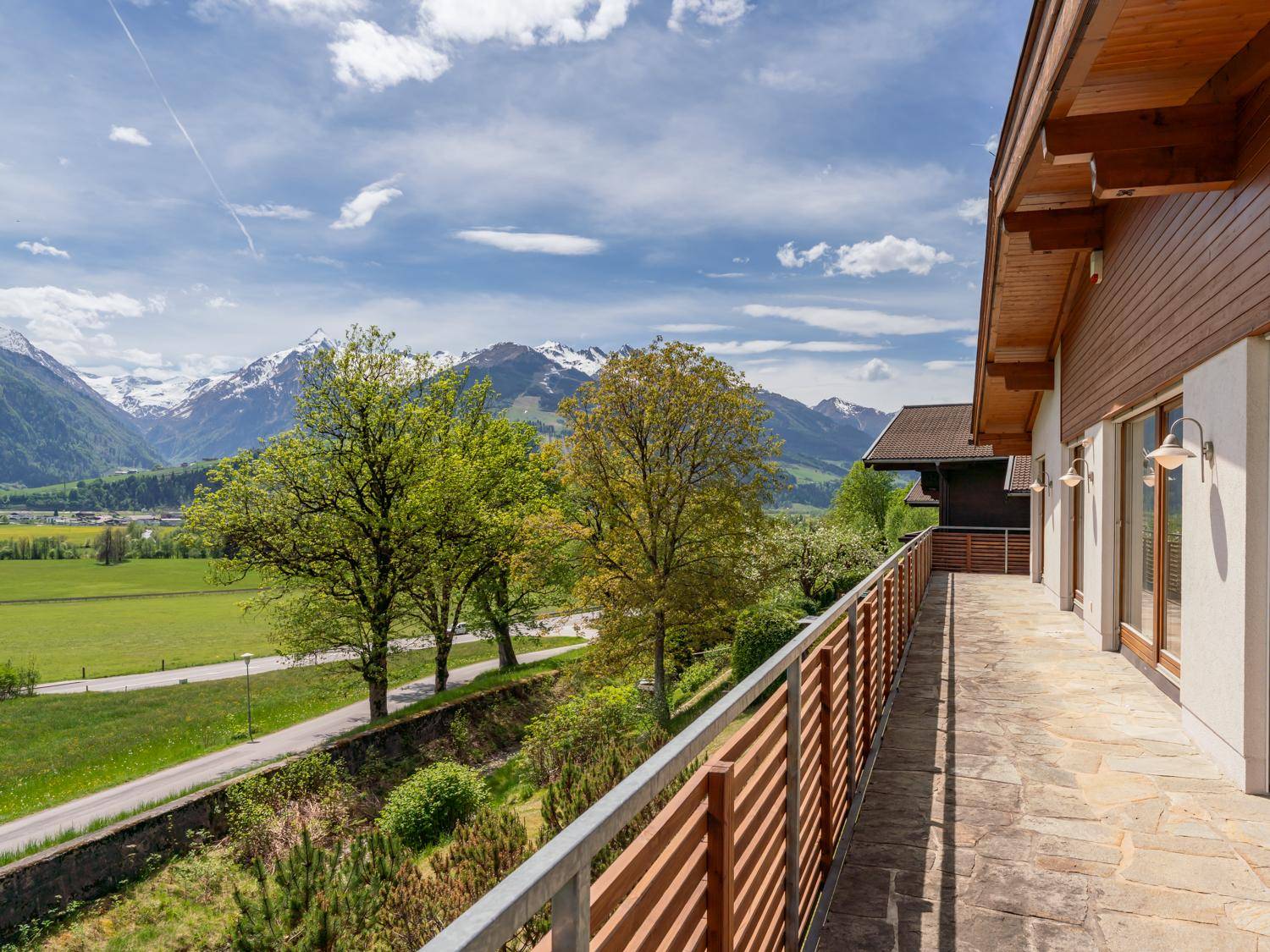 Langer Balkon mit Steinboden und weitem Blick über grüne Felder und Berge.