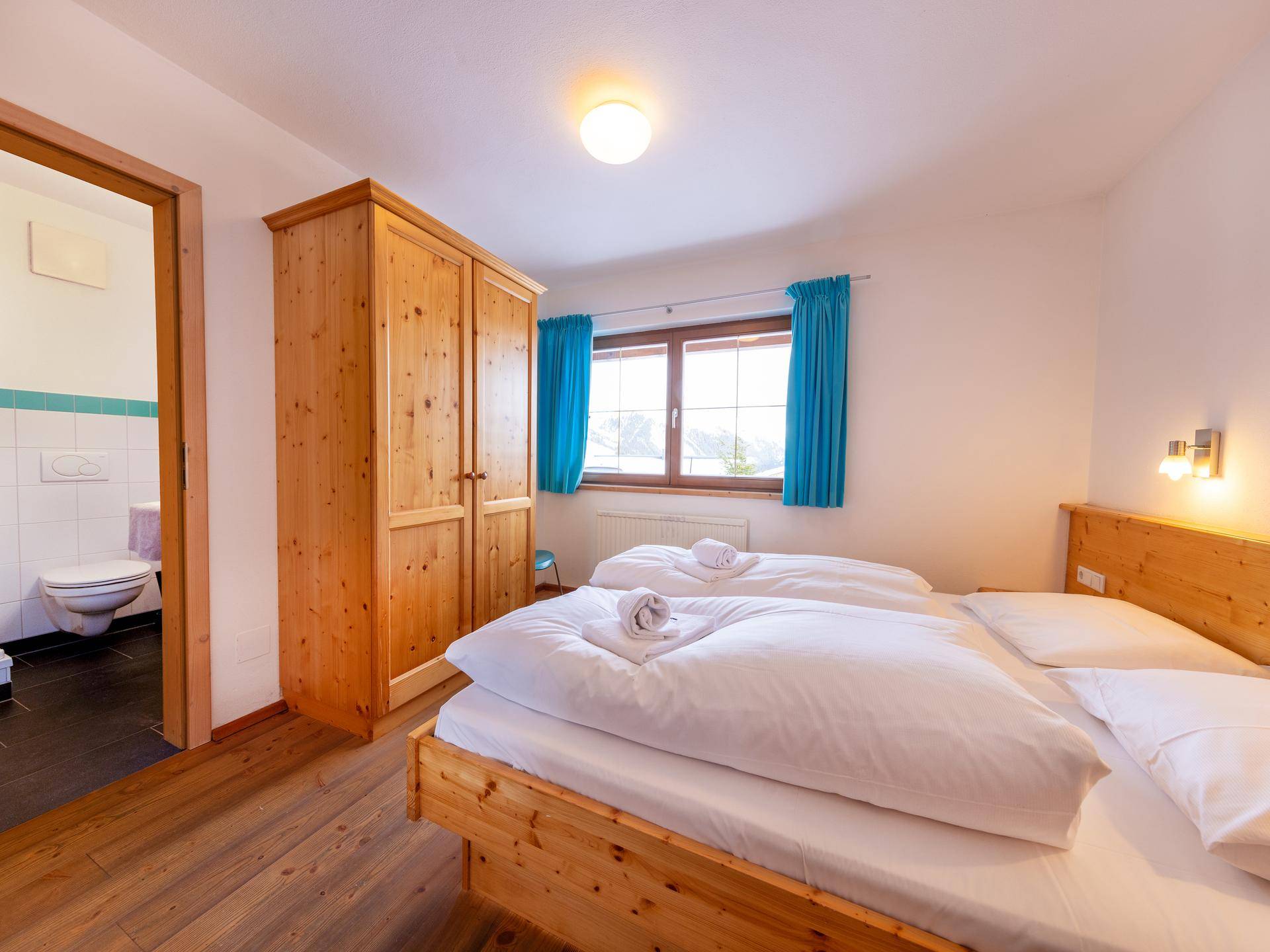 Schlafzimmer mit Holzbetten, Kleiderschrank und direktem Zugang zum Badezimmer.
