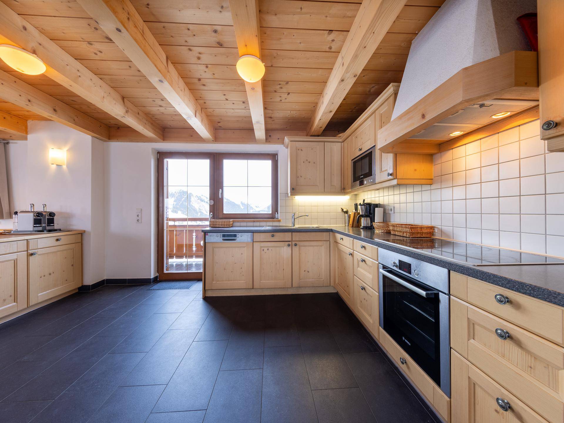 Helle Holzküche mit modernen Geräten, dunklem Fliesenboden und Zugang zum Balkon.