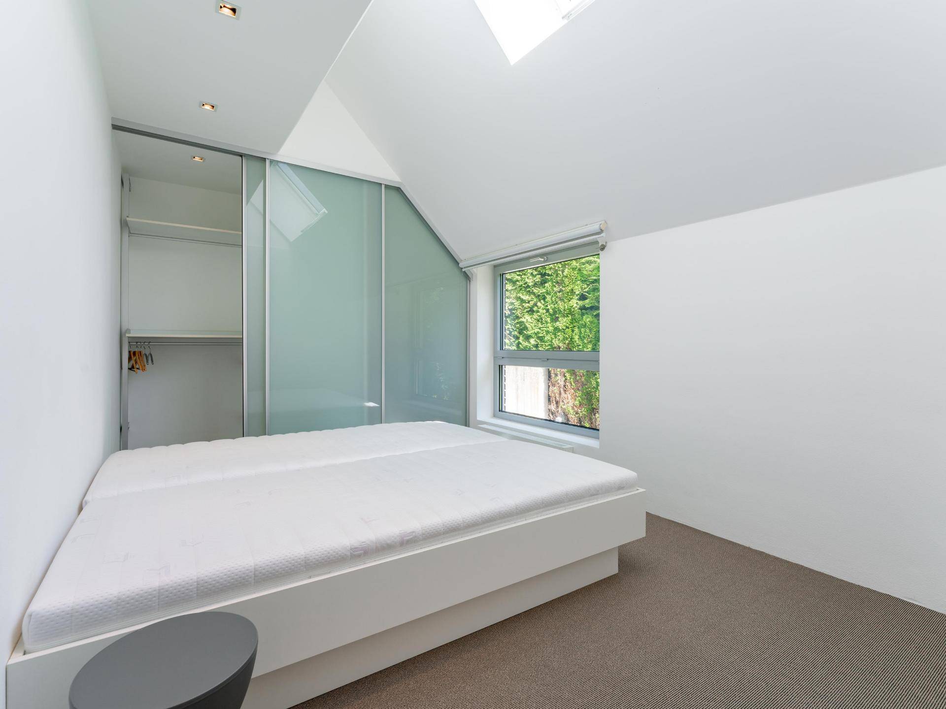 Helles Schlafzimmer mit modernem Bett, Einbauschränken und Dachfenster für viel Tageslicht.
