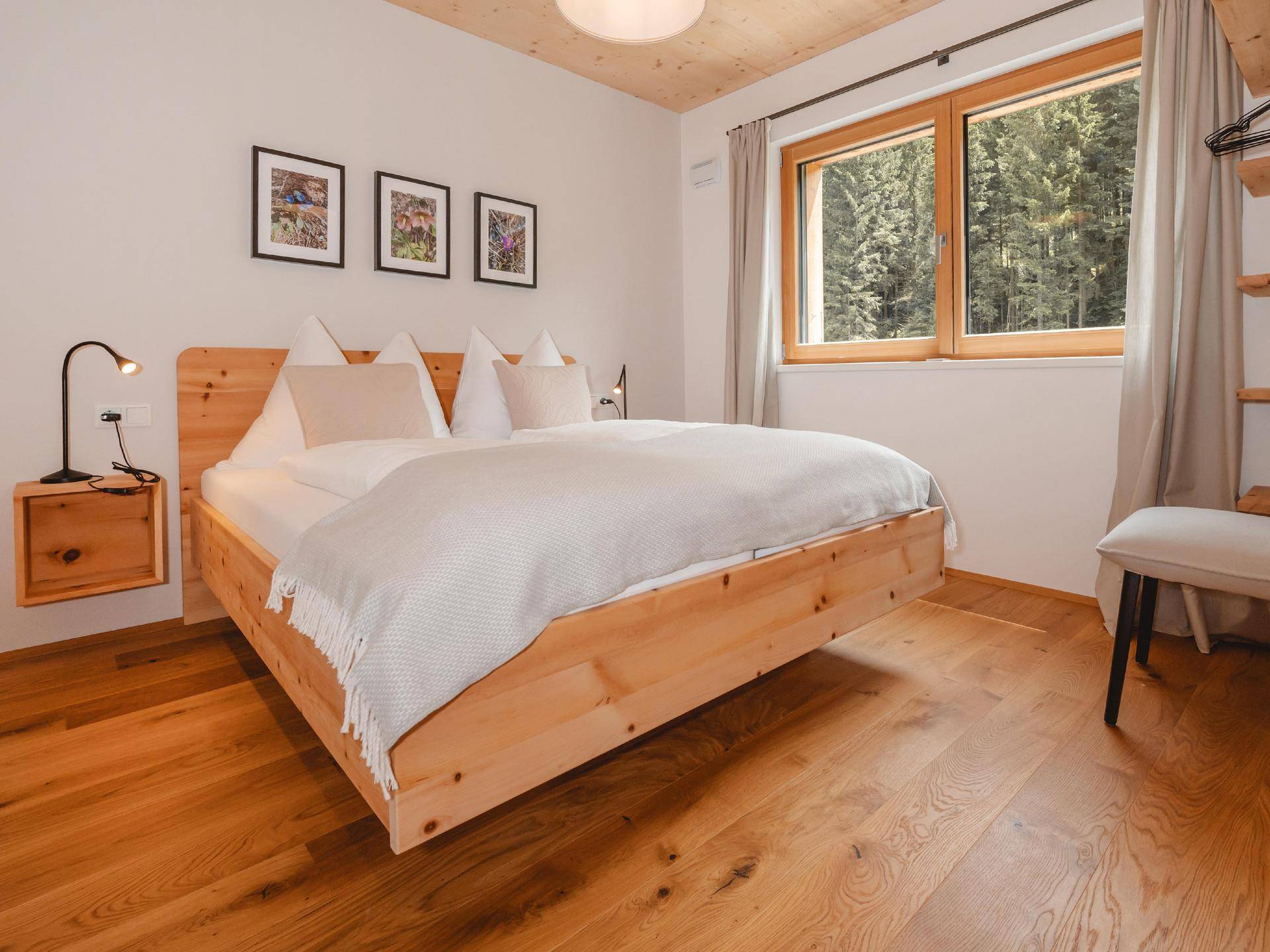 Gemütliches Schlafzimmer mit Holzbett, Eichenparkett und Blick ins Grüne durch große Fenster.