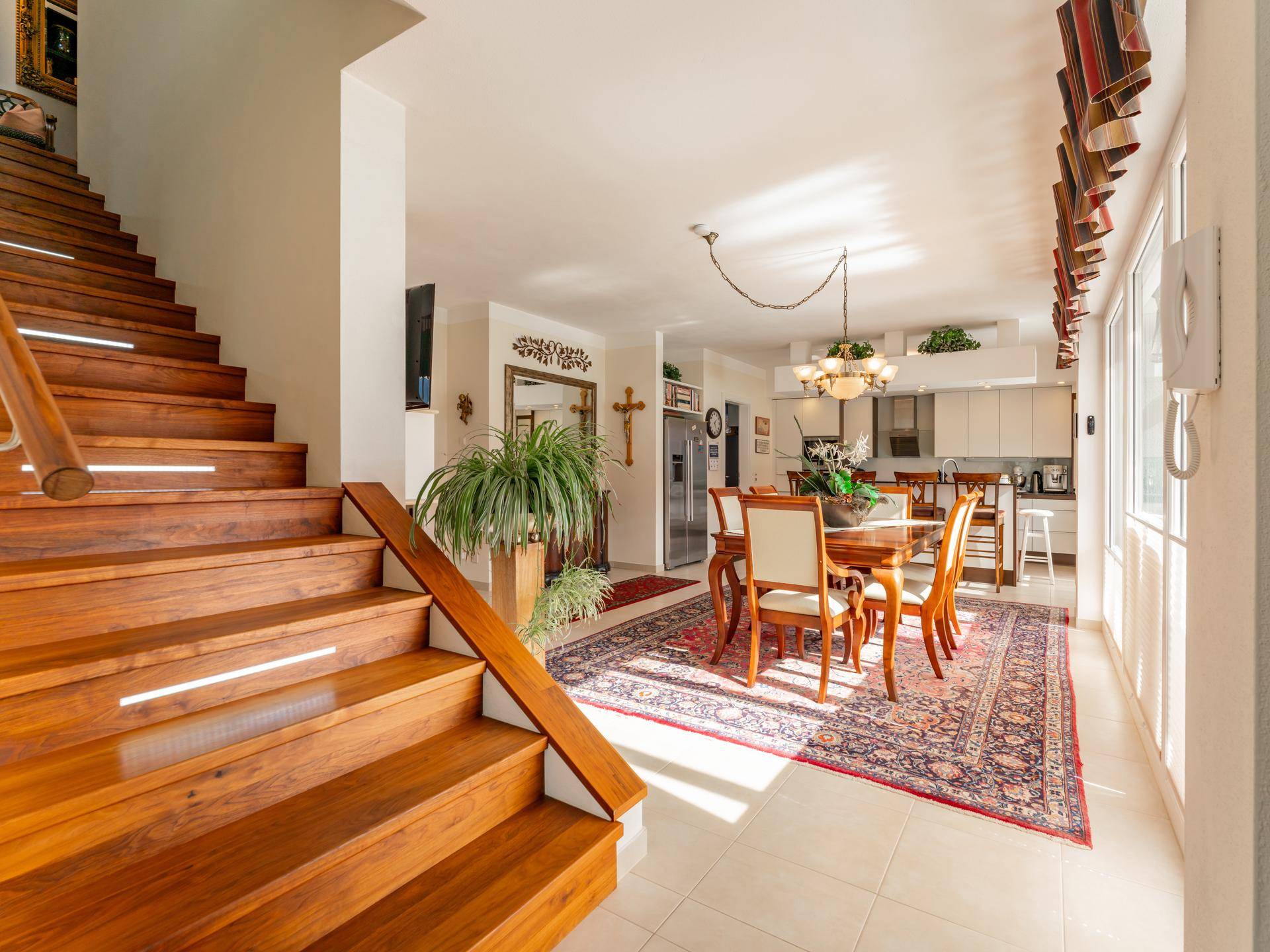Geräumiger Wohn-Essbereich mit eleganter Holztreppe, Teppich und offener Küche im Hintergrund.