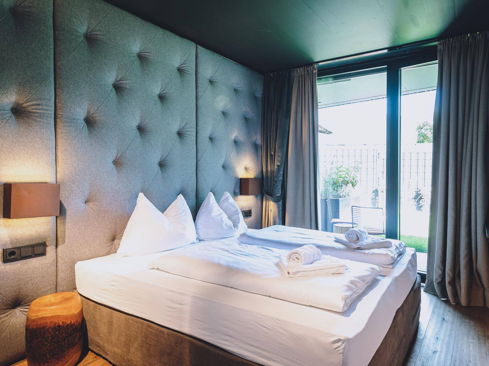 Gemütliches Schlafzimmer mit gepolstertem Kopfteil, Holzboden und Zugang zu einem privaten Außenbereich.
