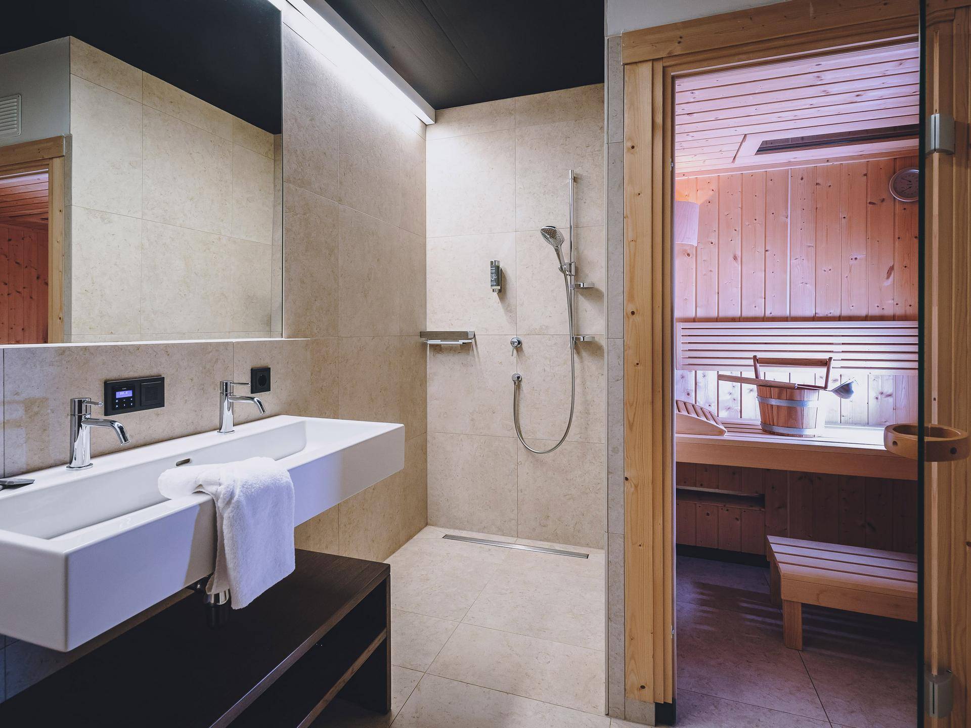 Modernes Badezimmer mit Doppelwaschbecken, ebenerdiger Dusche und direktem Zugang zur privaten Sauna.
